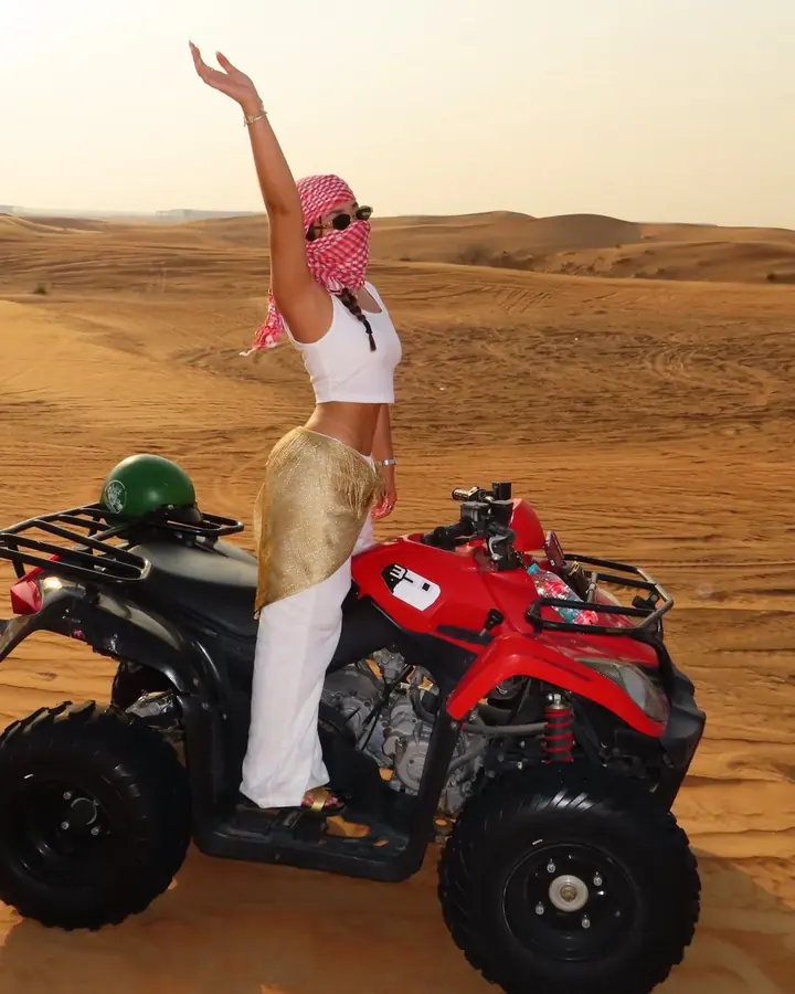 Guest standing on a red quad bike and waving on the dunes