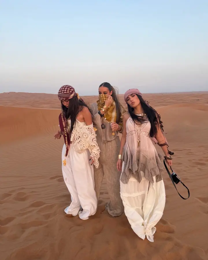 Three friends in light outfits and headscarves on the high red dunes