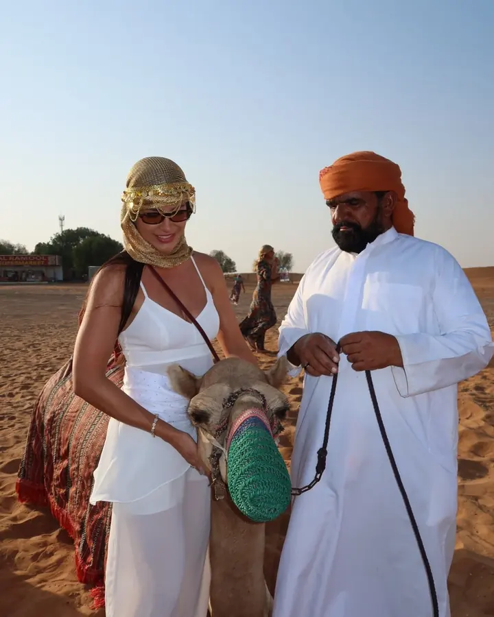 Guest stroking a camel next to the camel handler in traditional dress