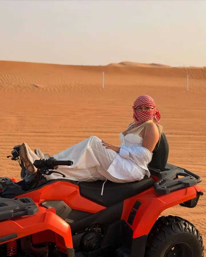 Guest relaxing on an orange quad bike in front of the dunes