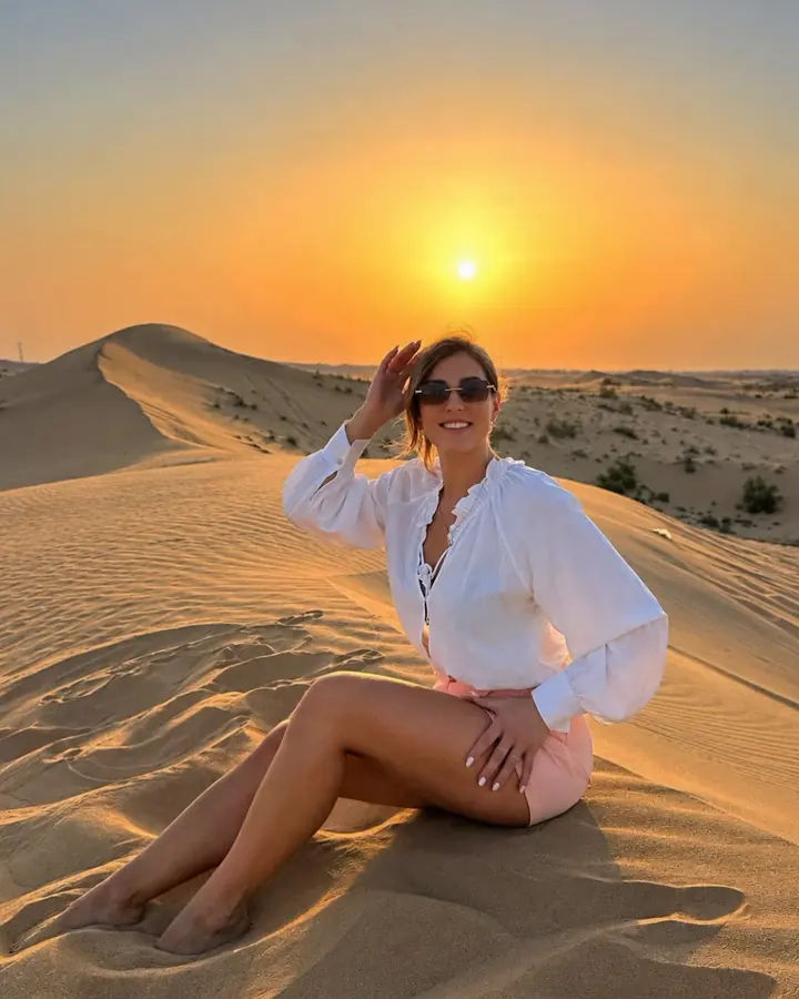 Guest sitting on a sand dune as the sun sets over the Dubai desert