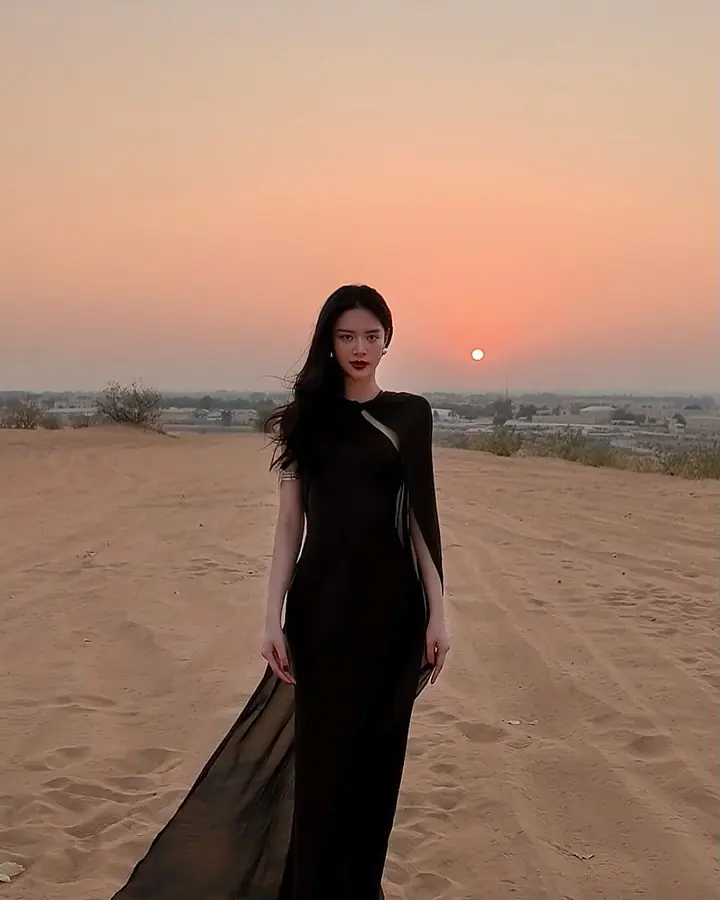 Guest in a long black dress standing on the sand at sunset