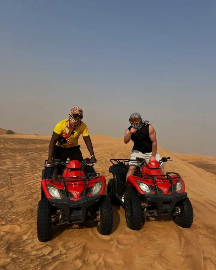 Two friends on red quad bikes on top of a dune