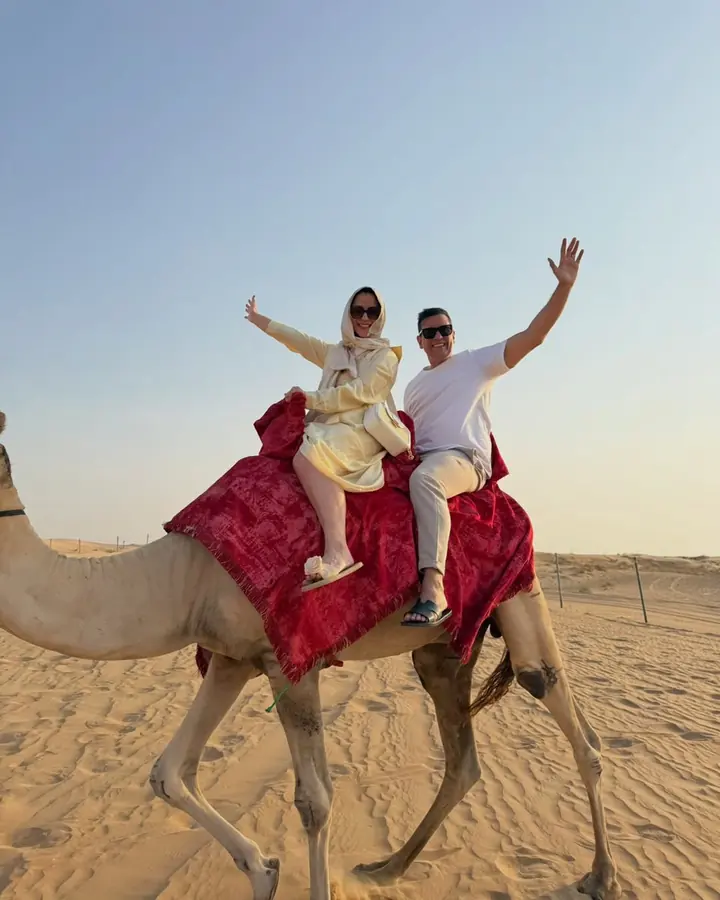 Couple riding a camel together and raising their arms