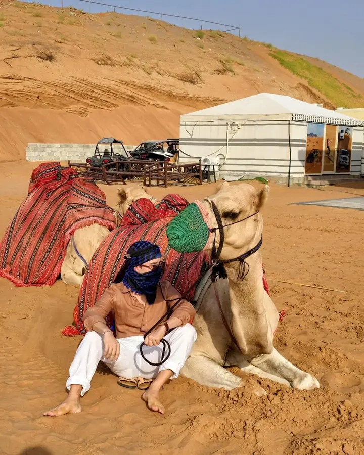 Guest resting beside a camel, with the camp tent and buggies behind