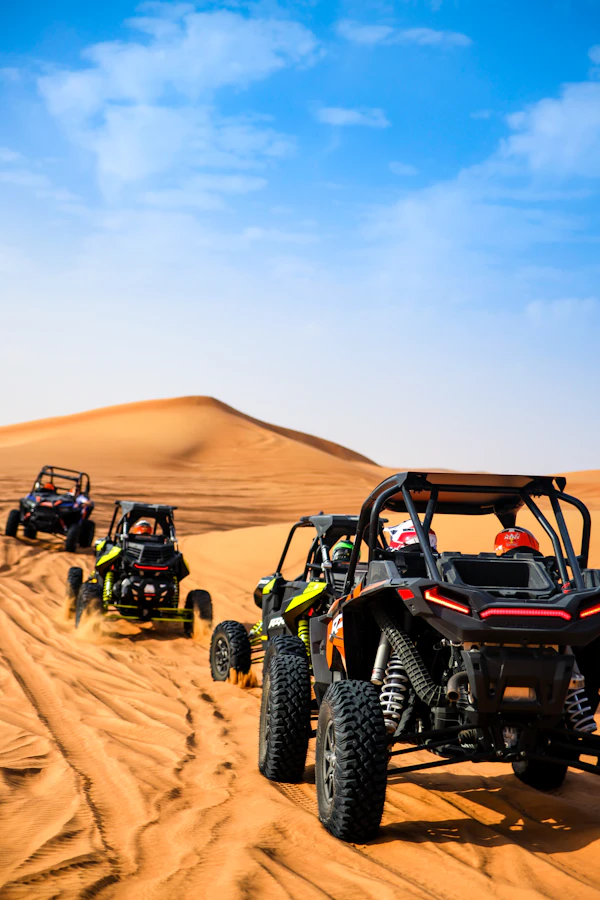 Group of dune buggies kicking up red sand while riders race through the Dubai desert